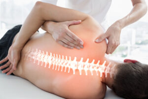 A male laying on his right side on top of a treatment table. His spine is illustrated on his back. A chiropractor is giving him treatment.